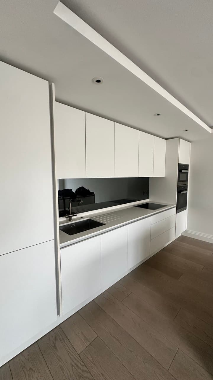 Completed kitchen with handleless cabinetry, smoked glass splashback, and engineered oak flooring
